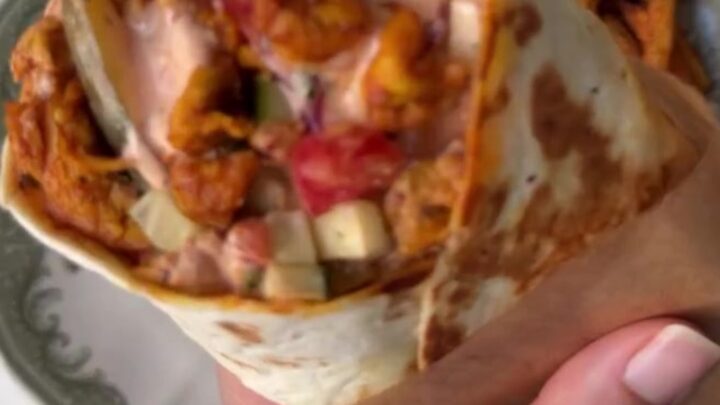 A golden toasted chicken shawarma wrap cut in half, showing spiced chicken, fries, and garlic sauce.
