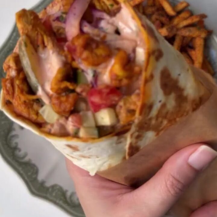 A golden toasted chicken shawarma wrap cut in half, showing spiced chicken, fries, and garlic sauce.