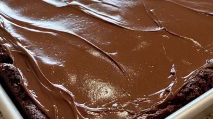 A close-up of a classic Texas sheet cake in a metal pan, topped with a smooth, glossy chocolate fudge icing.