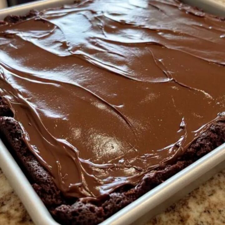A close-up of a classic Texas sheet cake in a metal pan, topped with a smooth, glossy chocolate fudge icing.