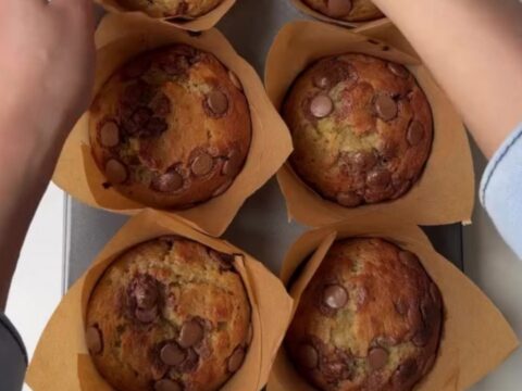 Giant bakery-style banana chocolate chip muffins with tall golden domes and melted chocolate chips on top, on a cooling rack.