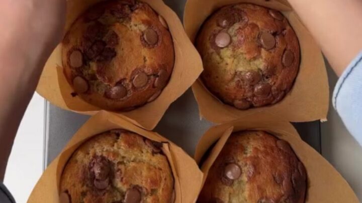 Giant bakery-style banana chocolate chip muffins with tall golden domes and melted chocolate chips on top, on a cooling rack.