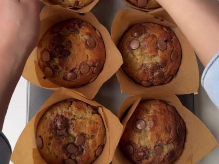 Giant bakery-style banana chocolate chip muffins with tall golden domes and melted chocolate chips on top, on a cooling rack.