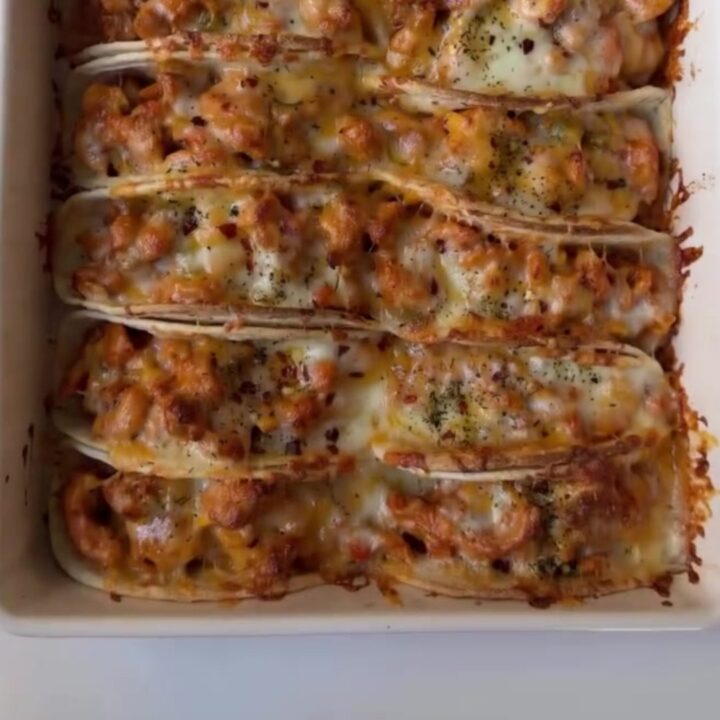 Golden crispy baked chicken tacos on a platter with a bowl of cilantro lime crema for dipping.