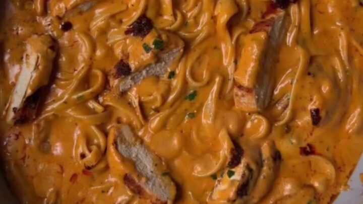 A fork twirling creamy chili crisp chicken Alfredo pasta with golden chicken slices and red chili oil ribbons.