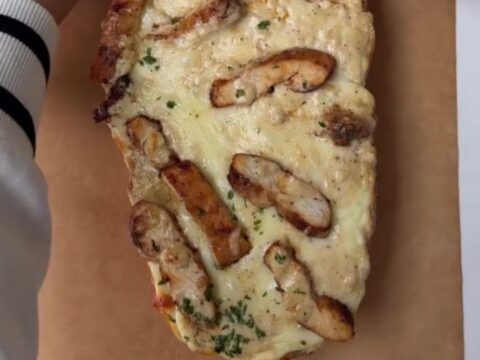 Cheesy chicken Alfredo garlic bread on a baking sheet, with melted mozzarella stretching as a slice is pulled away.