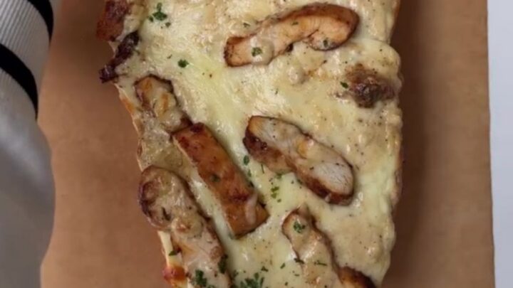 Cheesy chicken Alfredo garlic bread on a baking sheet, with melted mozzarella stretching as a slice is pulled away.