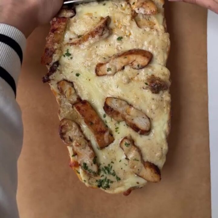 Cheesy chicken Alfredo garlic bread on a baking sheet, with melted mozzarella stretching as a slice is pulled away.