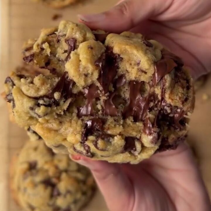 A thick, golden chocolate chip cookie broken open, showing a gooey