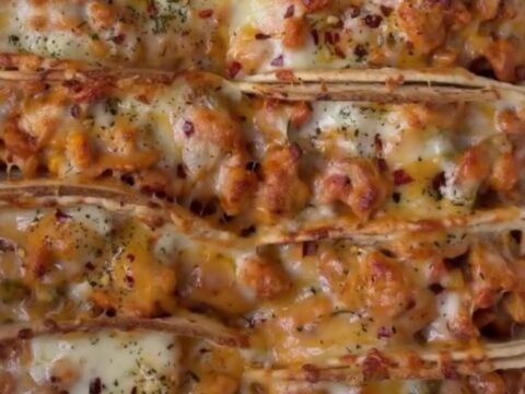 Golden crispy baked chicken tacos on a baking sheet, with a bowl of cilantro crema for dipping