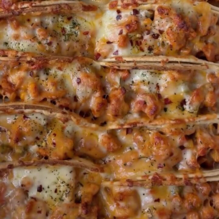 Golden crispy baked chicken tacos on a baking sheet, with a bowl of cilantro crema for dipping