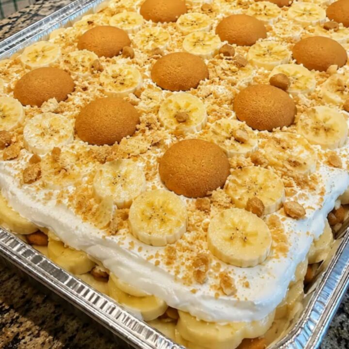 A large aluminum pan filled with layered banana pudding topped with vanilla wafers and banana slices.