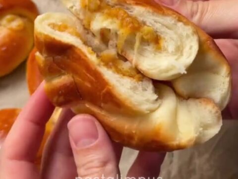 Golden Turkish poğaça buns on a parchment-lined baking sheet, one torn open showing cheese pull