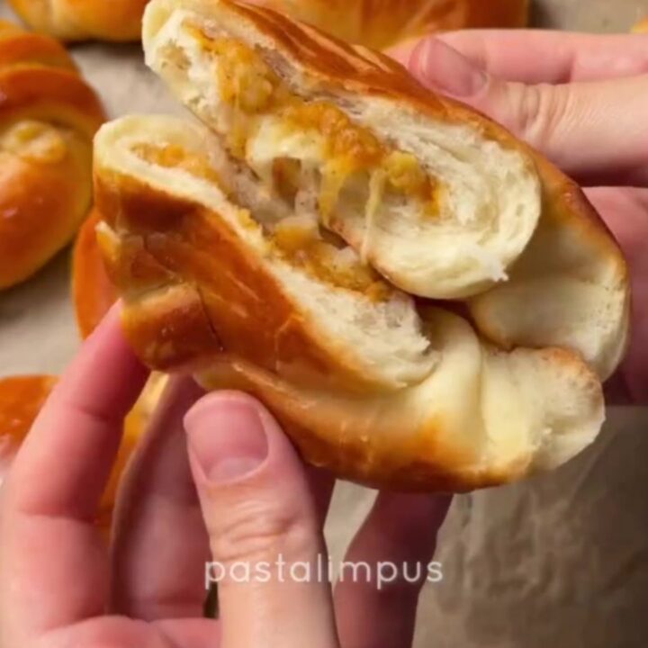 Golden Turkish poğaça buns on a parchment-lined baking sheet, one torn open showing cheese pull