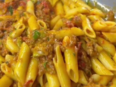 Golden penne pasta with meatballs, roasted tomatoes, and zucchini in a skillet, topped with melted cheese and parsley.