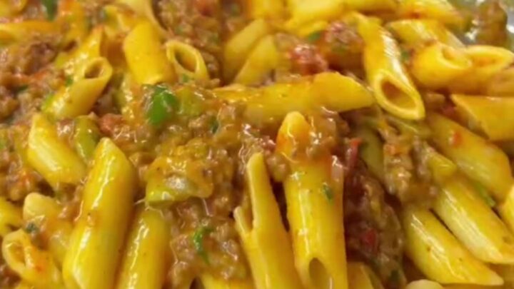 Golden penne pasta with meatballs, roasted tomatoes, and zucchini in a skillet, topped with melted cheese and parsley.