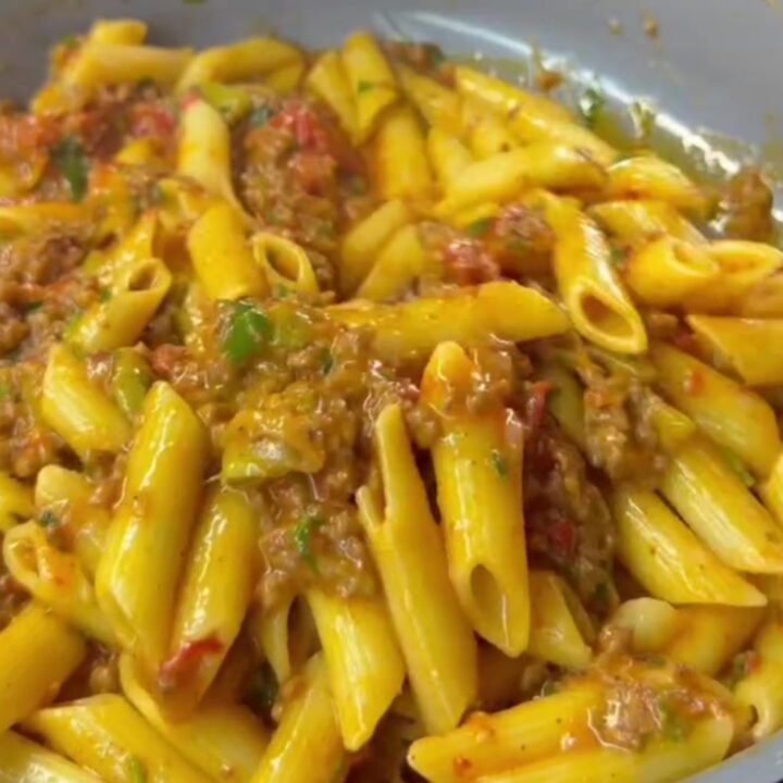 Golden penne pasta with meatballs, roasted tomatoes, and zucchini in a skillet, topped with melted cheese and parsley.