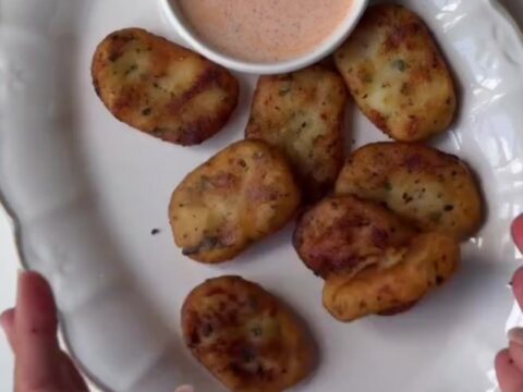 Golden crispy potato nuggets piled on a plate with ketchup