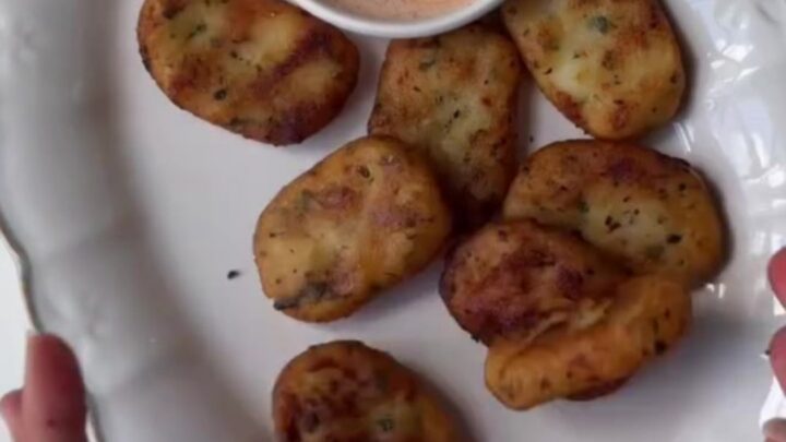 Golden crispy potato nuggets piled on a plate with ketchup