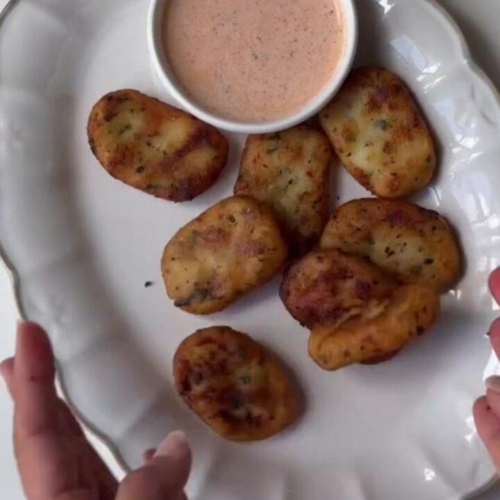 Golden crispy potato nuggets piled on a plate with ketchup