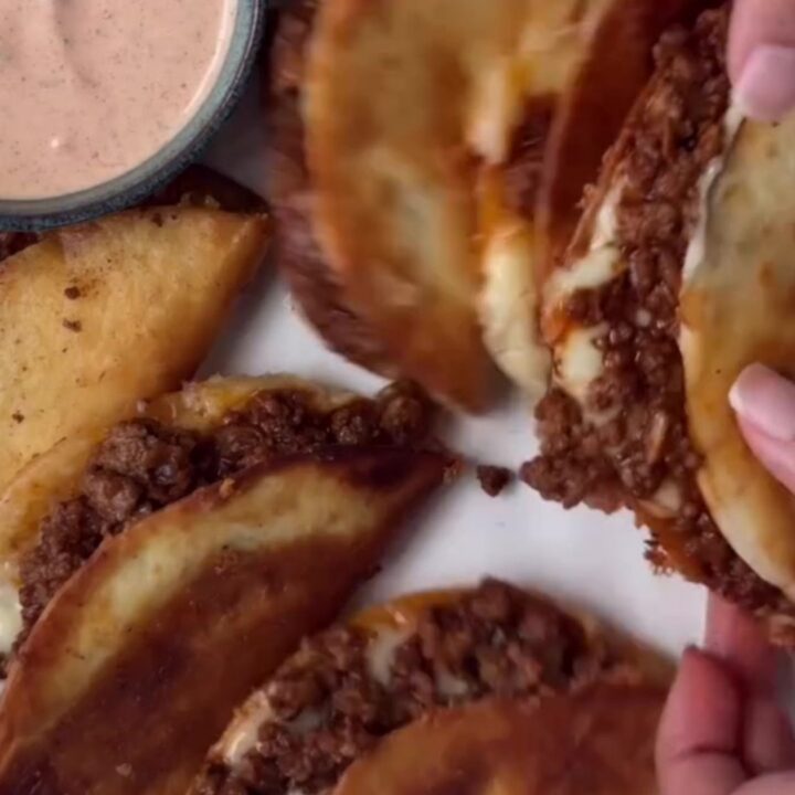 Golden crispy beef tacos topped with pico de gallo and drizzled with creamy taco sauce on a rustic plate