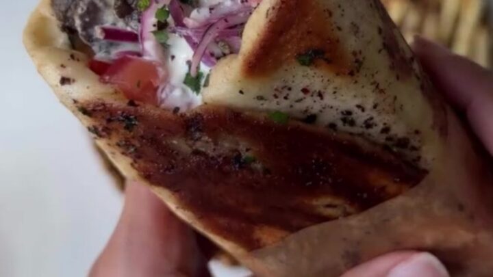 Crispy pomegranate-glazed ribeye shawarma wrap sliced in half, showing juicy beef, fries, and pink onions.