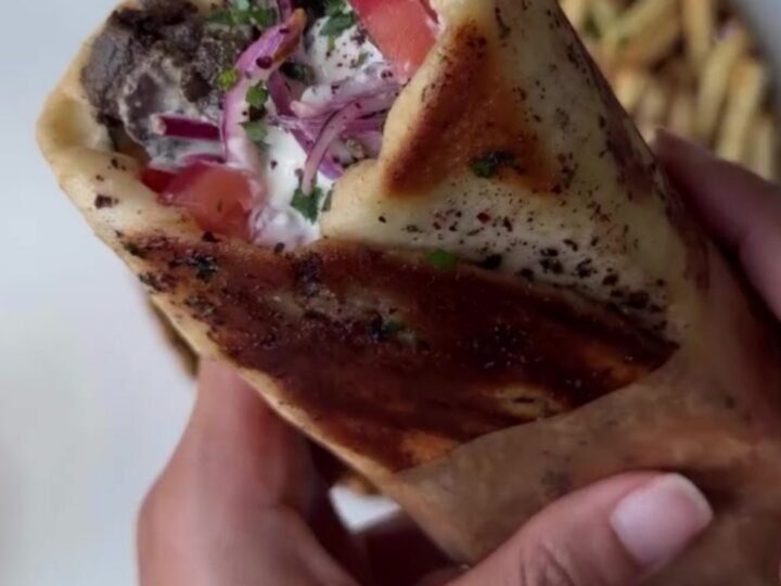 Crispy pomegranate-glazed ribeye shawarma wrap sliced in half, showing juicy beef, fries, and pink onions.