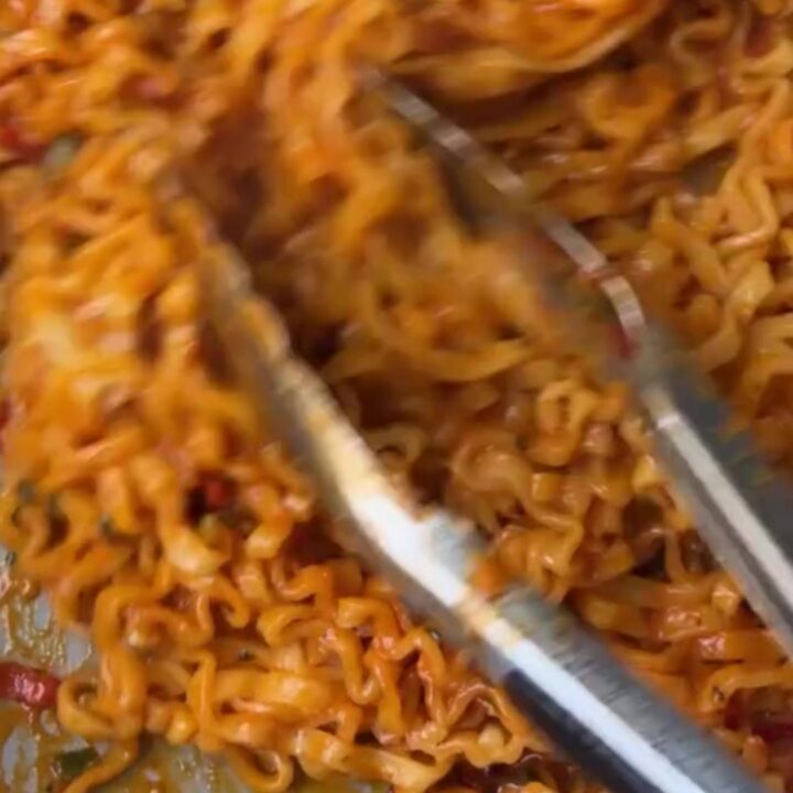 A bowl of spicy garlic chili oil ramen topped with scallions, cilantro, and lime wedges