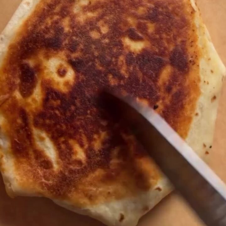 Golden hexagonal Crunchwrap Supreme cut in half showing layers of beef, cheese, tostada, and lettuce.