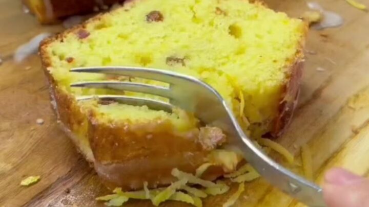 Sliced whole lemon loaf cake with dried fruit on a wooden board