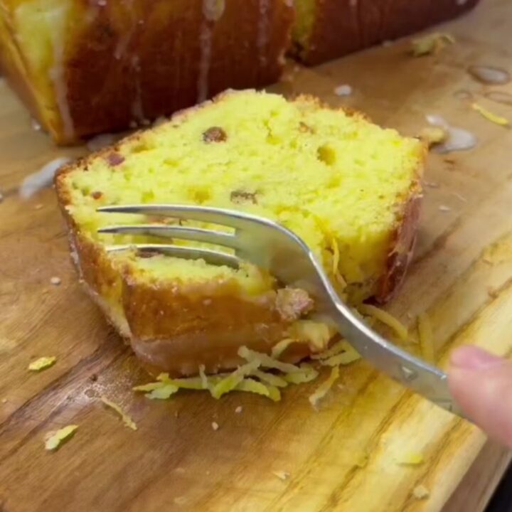 Sliced whole lemon loaf cake with dried fruit on a wooden board