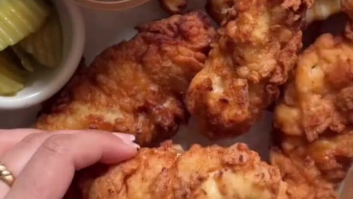Crispy golden chicken tenders piled on a wire rack with a bowl of Cane's sauce for dipping