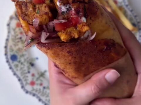 Crispy chicken shawarma wrap sliced in half, showing layers of chicken, fries, onions, and toum, with a side of garlic sauce.