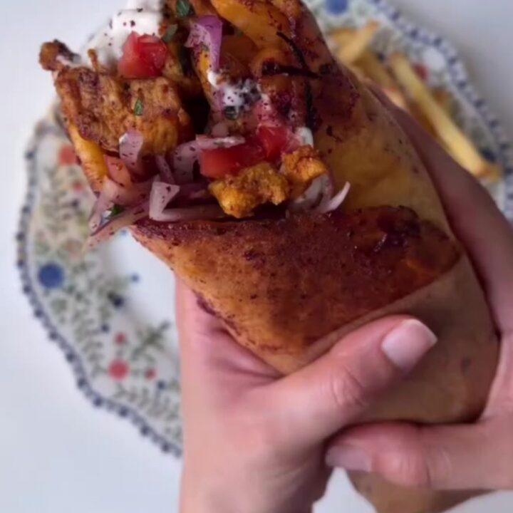 Crispy chicken shawarma wrap sliced in half, showing layers of chicken, fries, onions, and toum, with a side of garlic sauce.