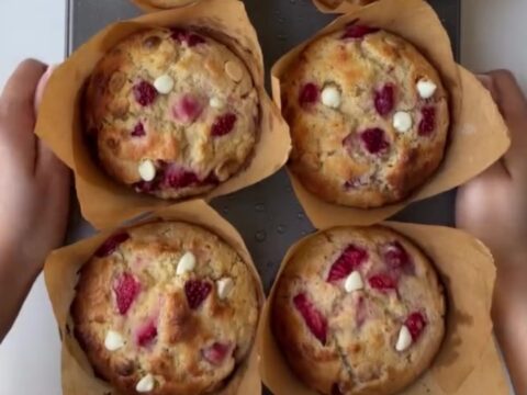 Golden-domed muffin broken open showing molten white chocolate and roasted strawberries