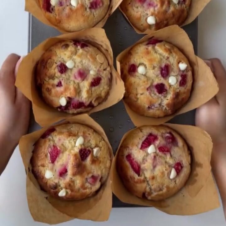 Golden-domed muffin broken open showing molten white chocolate and roasted strawberries