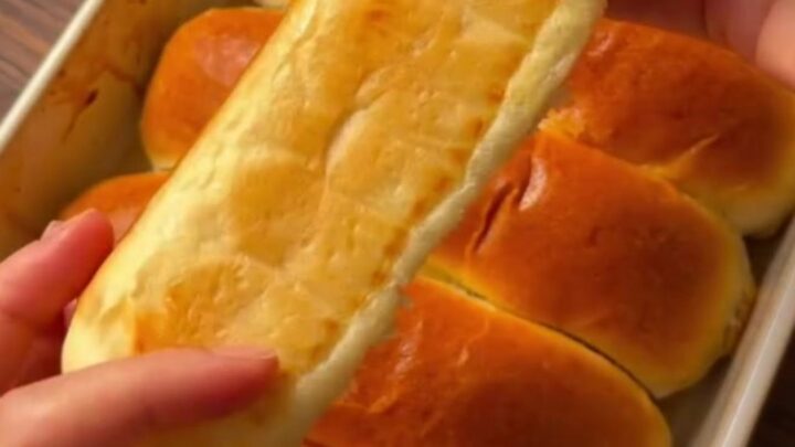 Golden brown homemade sandwich buns on a baking sheet, brushed with butter