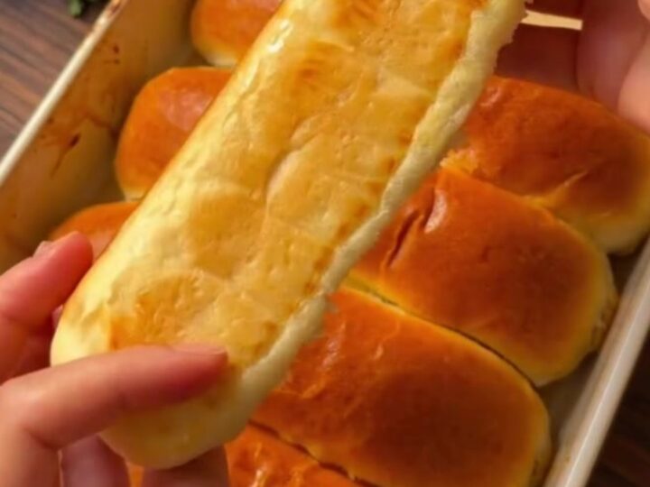 Golden brown homemade sandwich buns on a baking sheet, brushed with butter