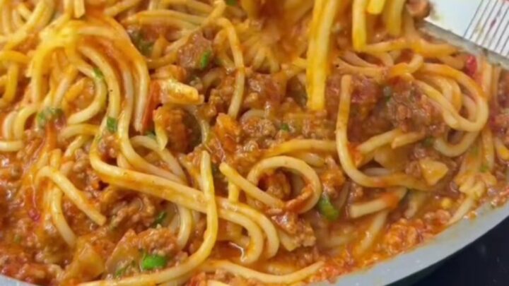 A fork twirling spaghetti with blistered vine tomatoes and ground beef in a skillet