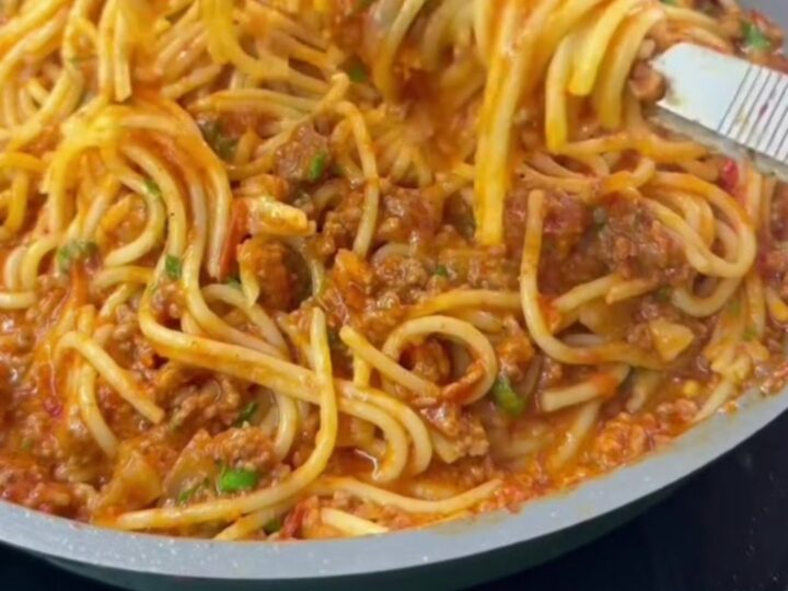 A fork twirling spaghetti with blistered vine tomatoes and ground beef in a skillet