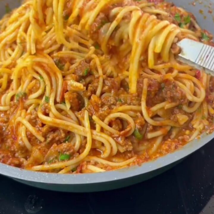 A fork twirling spaghetti with blistered vine tomatoes and ground beef in a skillet