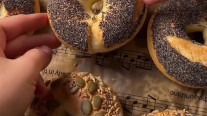 Golden seed-crusted bagels on a wire rack, with one split and spread with cream cheese