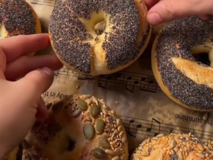 Golden seed-crusted bagels on a wire rack, with one split and spread with cream cheese