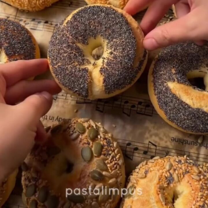 Golden seed-crusted bagels on a wire rack, with one split and spread with cream cheese