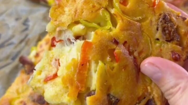 Golden sheet pan crepe pizza topped with sucuk, corn, peppers, and melted mozzarella, cut into squares