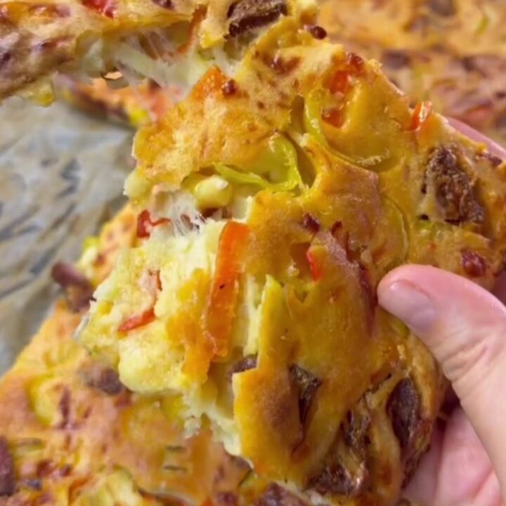 Golden sheet pan crepe pizza topped with sucuk, corn, peppers, and melted mozzarella, cut into squares