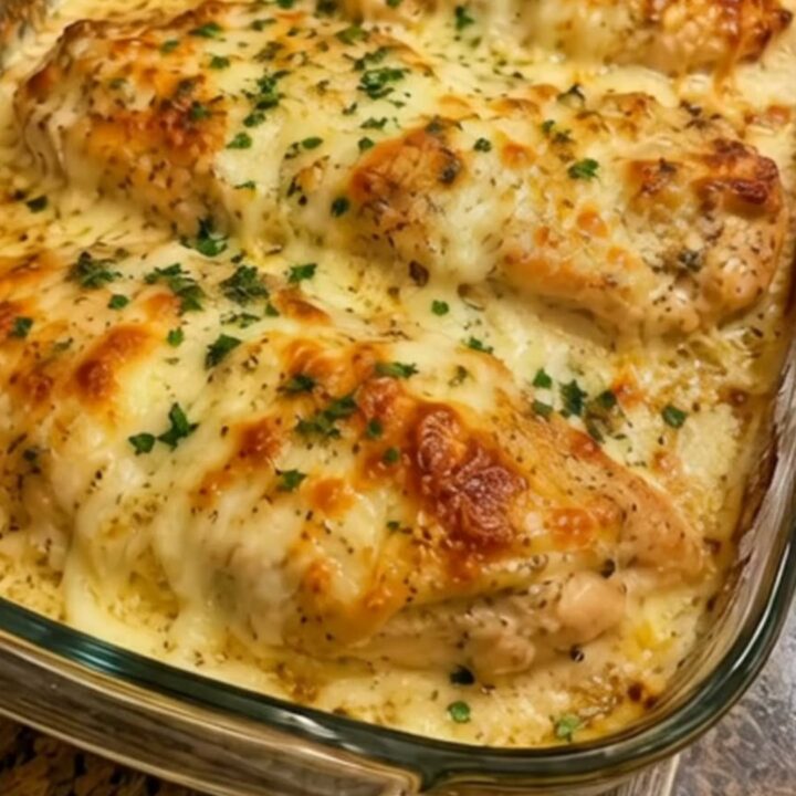 A close-up of a spatula lifting a juicy chicken breast from a glass dish with a long mozzarella cheese pull.