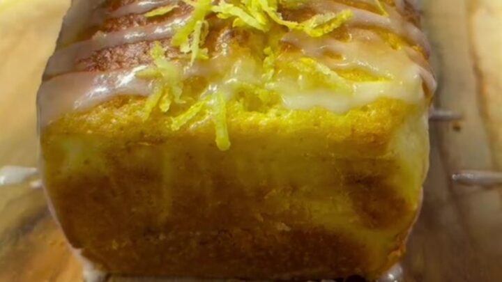 Golden lemon loaf cake with white glaze and lemon zest on a cooling rack