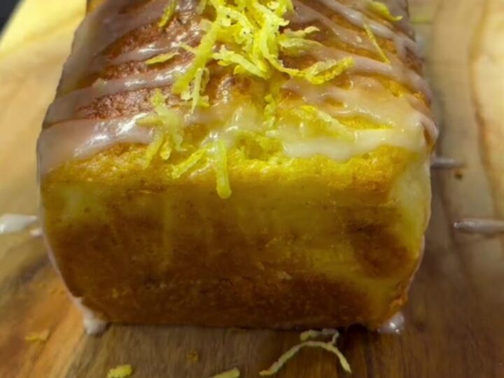 Golden lemon loaf cake with white glaze and lemon zest on a cooling rack