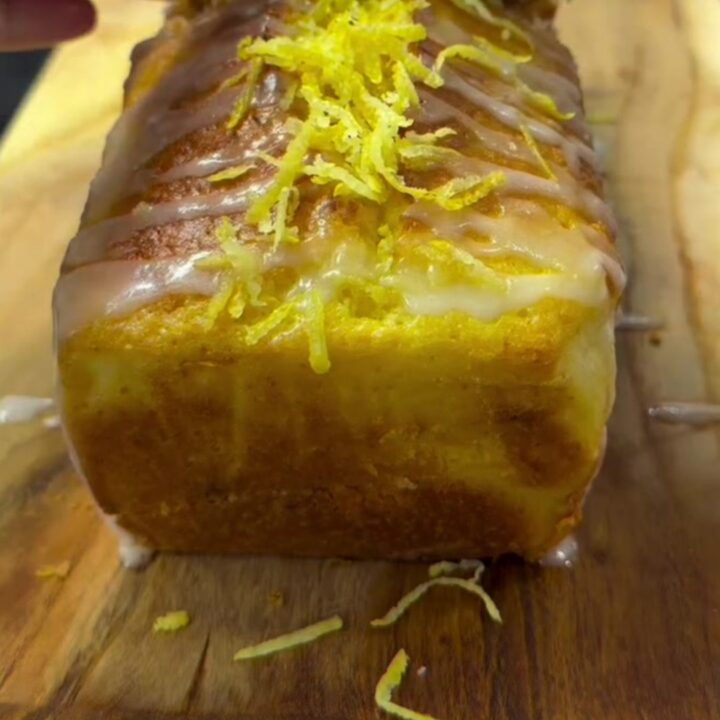 Golden lemon loaf cake with white glaze and lemon zest on a cooling rack